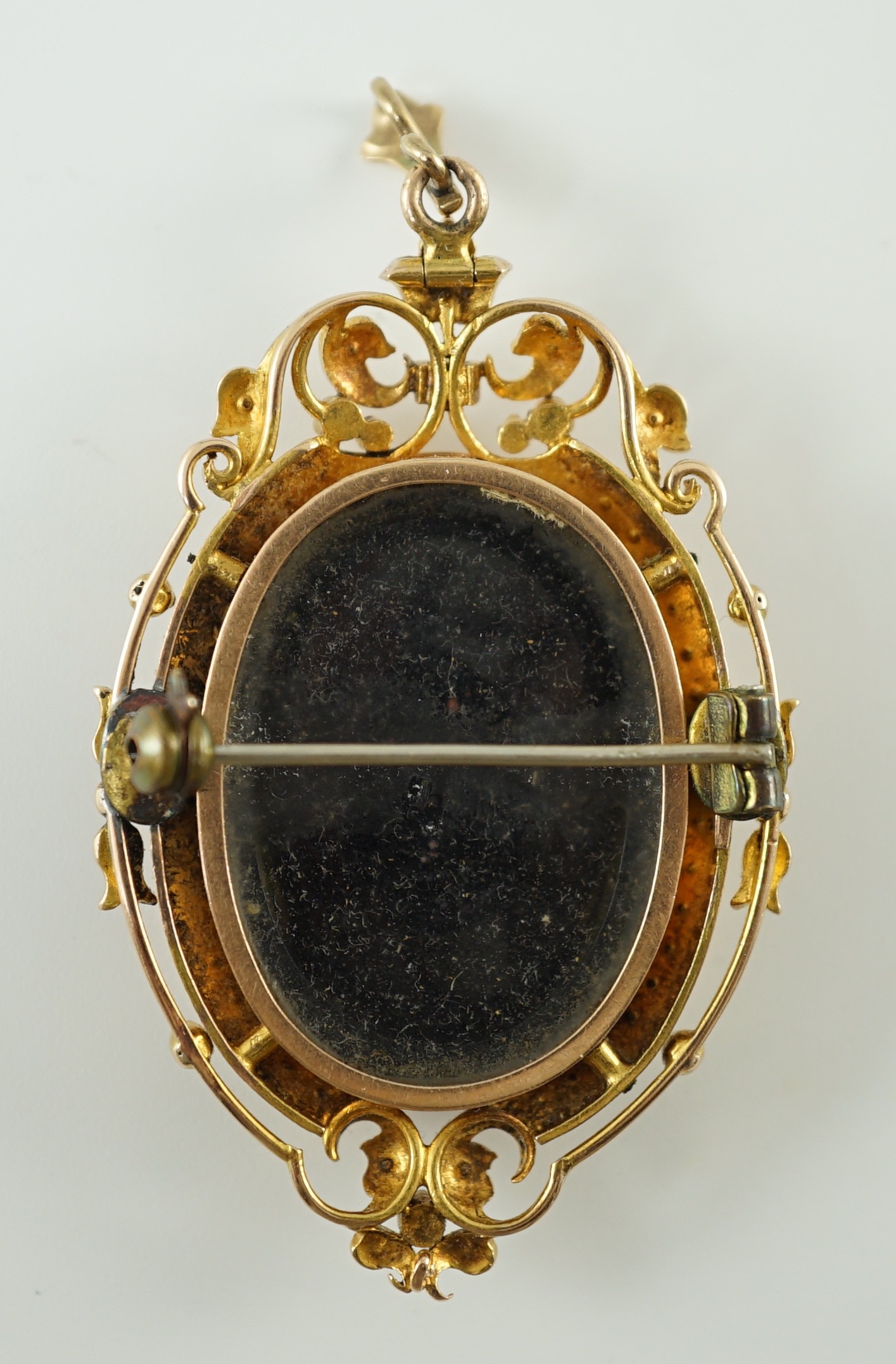 A Victorian oval gold and enamel pendant/brooch, painted with a cherub offering cherries to a dove, within a black and split pearl outer border